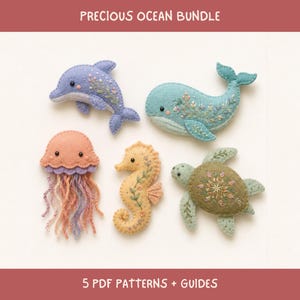 May include: A Precious Ocean Bundle featuring five felt sea creatures: a lavender dolphin, a light blue whale, a peach jellyfish with yarn tentacles, a yellow seahorse, and a green sea turtle. Each figure displays intricate floral embroidery.
