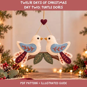 May include: A felt ornament featuring two cream-colored turtle doves perched on a brown branch. The birds have light blue wings with red leaf embroidery and dark red tail feathers. A small dark red heart hangs above the birds. Text reads: TWELVE DAYS OF CHRISTMAS DAY TWO: TURTLE DOVES PDF PATTERN + ILLUSTRATED GUIDE.