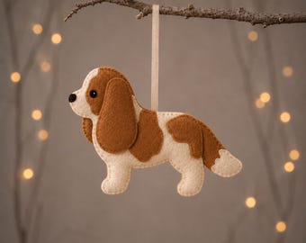 May include: A felt Cavalier King Charles Spaniel ornament in cream and brown, hanging from a light ribbon. The text CAVALIER KING CHARLES SPANIEL appears at the top, with PDF & SVG PATTERN + GUIDE | 2 SIZES printed at the bottom of the image.