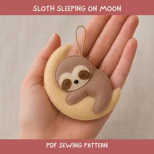 May include: A felt ornament featuring a light brown sloth sleeping on a pale yellow crescent moon. The sloth has dark brown eye patches and a small black nose. A thin brown string loop is attached to the top. Text reads: SLOTH SLEEPING ON MOON PDF SEWING PATTERN.