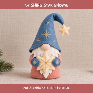 Puede incluir: Una figura de gnomo de fieltro con un sombrero azul puntiagudo con estrellas doradas bordadas y una estrella colgante en la punta. El gnomo tiene una nariz color melocotón, barba blanca y cuerpo rosa, sosteniendo una gran estrella color crema. El texto dice WISHING STAR GNOME PDF SEWING PATTERN + TUTORIAL.