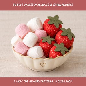 May include: A cream-colored bowl with a small heart icon contains 3D felt marshmallows in white and pink, alongside red felt strawberries with green leaves. Text reads: 3D FELT MARSHMALLOWS & STRAWBERRIES and 2 EASY PDF SEWING PATTERNS | 3 SIZES EACH.