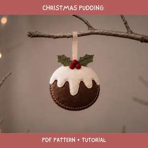 May include: A felt Christmas pudding ornament featuring a dark brown base, a white icing top, and green holly leaves with three red berries. The ornament hangs from a beige ribbon loop and includes the text CHRISTMAS PUDDING PDF PATTERN + TUTORIAL.