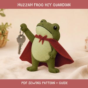 May include: A green felt frog figurine wearing a dark red cape with a bow tie at the neck. The frog holds a silver metal key in its raised right hand. The text HUZZAH FROG KEY GUARDIAN and PDF SEWING PATTERN + GUIDE is visible on the image.