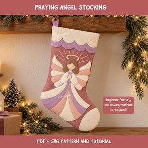Peut inclure: Une chaussette de Noël en feutrine représentant un ange en prière avec des cheveux bruns, une auréole dorée et des ailes superposées dans des tons crème, pêche et lavande. Elle possède un revers festonné crème et un corps rose poudré.