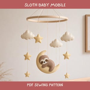 Op de afbeelding: Een babymobiel met een rond houten frame en hangende vilten elementen, waaronder een bruine luiaard op een crèmekleurige halve maan, crèmekleurige wolken en gele sterren. De tekst SLOTH BABY MOBILE en PDF SEWING PATTERN is zichtbaar.