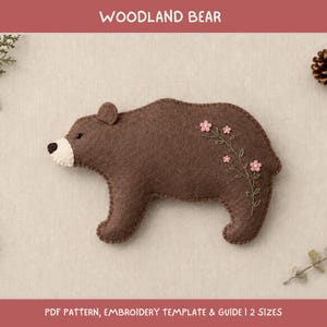 May include: A brown felt bear ornament featuring a cream-coloured snout, a black nose, and embroidered green stems with small pink flowers on its side. The text WOODLAND BEAR and PDF PATTERN, EMBROIDERY TEMPLATE & GUIDE | 2 SIZES is visible.
