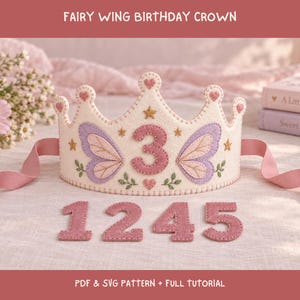 May include: A cream-colored felt birthday crown featuring embroidered purple fairy wings, small gold stars, and a central number 3. The crown includes pink ribbon ties and additional felt numbers 1, 2, 4, and 5. Text reads: FAIRY WING BIRTHDAY CROWN, PDF & SVG PATTERN + FULL TUTORIAL.