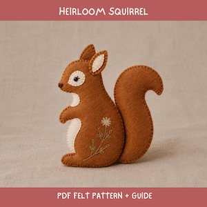 Puede incluir: Una ardilla de fieltro marrón con vientre e interior de las orejas de color crema, con un diseño de flor blanca bordada en el costado. El texto HEIRLOOM SQUIRREL y PDF FELT PATTERN + GUIDE aparece en blanco sobre un fondo rojo oscuro.