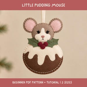 May include: A felt ornament shaped like a mouse emerging from a Christmas pudding, featuring brown and cream colours, pink inner ears, and green holly leaves with red berries. The text reads LITTLE PUDDING MOUSE and BEGINNER PDF PATTERN + TUTORIAL | 2 SIZES.