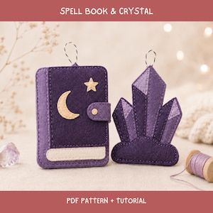 May include: A purple felt spell book ornament with a cream crescent moon and star, alongside a purple felt crystal cluster ornament. Both items feature a black and white hanging string. Text at the top reads SPELL BOOK & CRYSTAL.