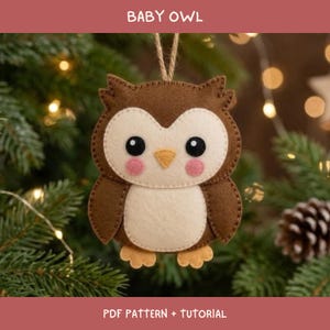 Puede incluir: Un adorno de fieltro con forma de búho en tonos marrón y crema, con ojos negros, pico amarillo y mejillas rosadas. El búho tiene un lazo para colgar y muestra el texto BABY OWL y PDF PATTERN + TUTORIAL en la parte inferior de la imagen.