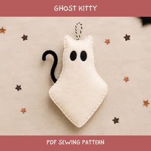 May include: A cream-colored felt ghost kitty ornament with black stitched eyes and a black pipe cleaner tail. The ornament features a black and white striped hanging loop at the top. The text GHOST KITTY and PDF SEWING PATTERN is visible.