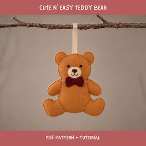 Könnte beinhalten: Ein brauner Teddybär-Anhänger aus Filz mit cremefarbener Schnauze, schwarzen Perlenaugen und einer dunkelroten Fliege. Der Bär hängt an einem hellbeigen Band und hat sichtbare Nähte an den Rändern. Der Text lautet CUTE N' EASY TEDDY BEAR.