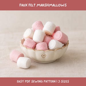 May include: A collection of cylindrical faux felt marshmallows in shades of white and soft pink, piled inside a cream-colored scalloped bowl featuring a small heart icon. The text FAUX FELT MARSHMALLOWS and EASY PDF SEWING PATTERN | 3 SIZES is visible.