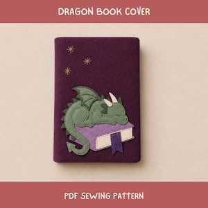 May include: A dark purple felt book cover featuring a green dragon appliqué resting on a light purple book with a cream-colored page edge and a dark purple bookmark. The cover includes three embroidered gold stars above the dragon. Text reads DRAGON BOOK COVER and PDF SEWING PATTERN.