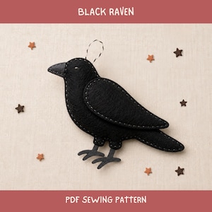 Op de afbeelding: Een zwart vilt ravenornament met zichtbare grijze stiksels, een klein lusje om op te hangen en verschillende kleine bruine en zwarte stervormige uitsparingen. De tekst BLACK RAVEN en PDF SEWING PATTERN is zichtbaar.