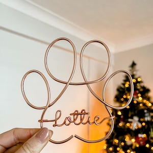 Può includere: Un'impronta di zampa in filo di ferro color oro rosa con il nome "Lottie" scritto in corsivo.