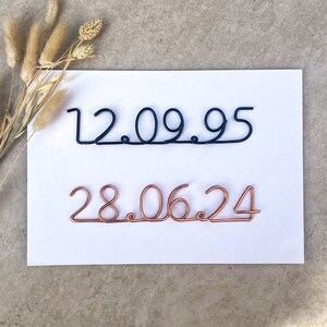 May include: Two wire sculptures of dates, 12.09.95 in black wire and 28.06.24 in copper wire, on a white background.