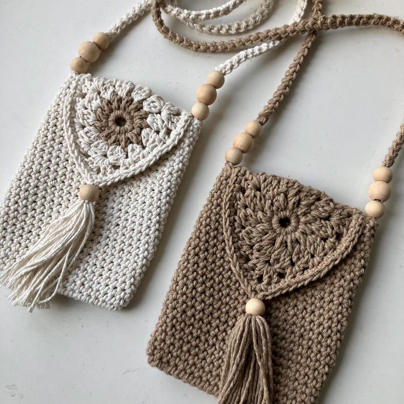 Puede incluir: Dos bolsos de tel&eacute;fono de ganchillo hechos a mano en crema y marr&oacute;n. Cada bolso presenta una solapa decorativa con un dise&ntilde;o floral, una borla y una correa de cuentas de madera. Los bolsos est&aacute;n dise&ntilde;ados para llevarse como bandolera.
