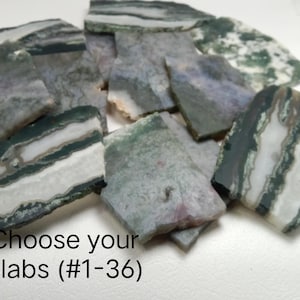 Puede incluir: Una colección de losas de piedra de forma irregular en tonos grises, verdes y blancos. Las losas tienen una apariencia en capas con vetas visibles. El texto de la imagen dice "Choose your Slabs (#1-36)".