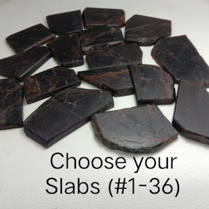 Op de afbeelding: Een verzameling donkerbruine, platte, onregelmatig gevormde stenen platen met zichtbare natuurlijke texturen en variaties. De tekst "Choose your Slabs (#1-36)" staat in het zwart onderaan de afbeelding gedrukt voor selectie.