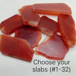 May include: A collection of translucent, reddish-orange carnelian stone slabs with smooth, polished surfaces and irregular shapes. The text "Choose your slabs (#1-32)" is printed in black at the bottom right of the image.