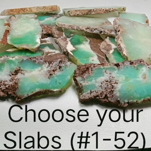 May include: A collection of raw, natural chrysoprase slabs with a vibrant green hue and brown matrix. The slabs have a rough, textured edge and are displayed on a white surface. Text on the image reads "Choose your Slabs (#1-52)".