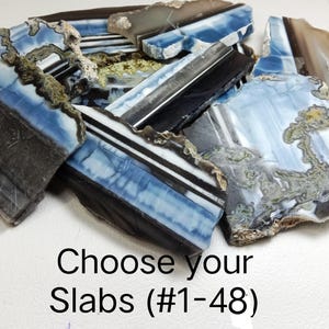 May include: A collection of irregular stone slabs featuring blue, white, black, and brown banded patterns with natural rough edges. The text Choose your Slabs (#1-48) is printed in black at the bottom of the image, indicating a selection of items.