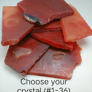 May include: A collection of flat, irregularly shaped red agate crystal slices with translucent and opaque sections, some featuring small druzy inclusions. The text "Choose your crystal (#1-36)" is printed in black at the bottom of the image.