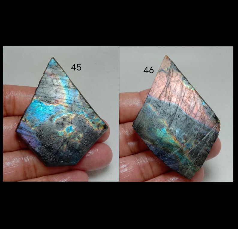 May include: Two iridescent labradorite gemstones, each held in a hand. The stones are roughly diamond-shaped, with a dark base color and flashes of blue, purple, and green. The number 45 is visible on the left stone, and 46 on the right.