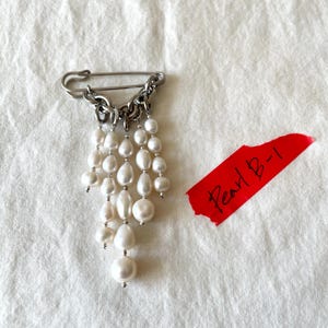 Spilla a forma di spilla da balia con perle, realizzata a mano, gioiello punk gotico di tendenza, spilla con catena pendente, accessorio di moda audace e d'avanguardia.