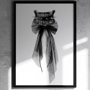 May include: Black and white framed print featuring a gothic-inspired design. The artwork showcases a black tulle bow and a studded collar. The image is set against a white background, with the text "MEKERA STUDIOS" at the bottom.