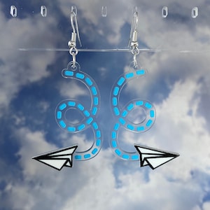 May include: A pair of blue and white acrylic earrings featuring a paper airplane design with a dotted line trail.