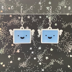 May include: A pair of blue and white earrings with a smiling face and wings. The earrings are made of plastic and have silver hooks.