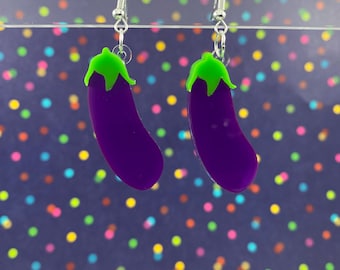 May include: A pair of eggplant-shaped earrings with green tops. The earrings are made of purple and green plastic and are hanging from silver hooks.