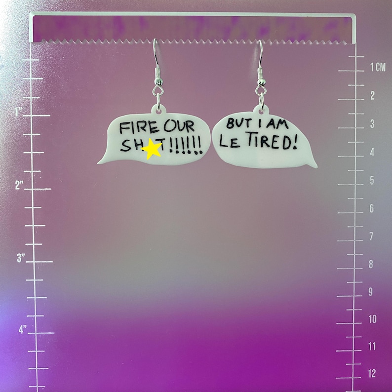 May include: White acrylic earrings in the shape of speech bubbles. One earring reads "FIRE OUR SH T!!!!!!" with a yellow star, and the other says "BUT I AM LE TIRED!" Silver-colored fish hook ear wires.
