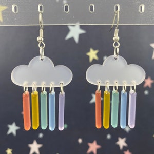 May include: A pair of earrings featuring a white cloud with a rainbow of colored raindrops hanging from it.
