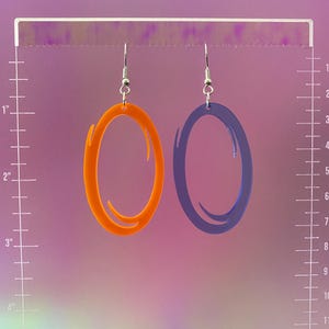 Puede incluir: Un par de pendientes con un dise&ntilde;o de portal. Un pendiente es naranja y el otro es azul.
