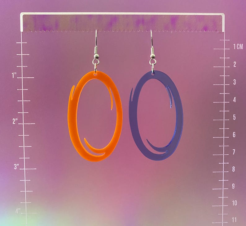 Puede incluir: Un par de pendientes con un dise&ntilde;o de portal. Un pendiente es naranja y el otro es azul.