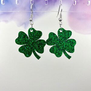 May include: A pair of green glitter four-leaf clover earrings with silver hooks.