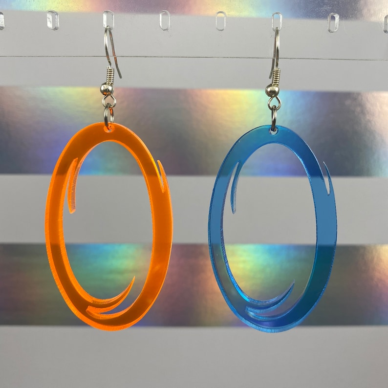 Puede incluir: Un par de pendientes con un dise&ntilde;o &uacute;nico. Los pendientes est&aacute;n hechos de acr&iacute;lico y tienen forma ovalada con un dise&ntilde;o de espiral. Un pendiente es naranja y el otro es azul.