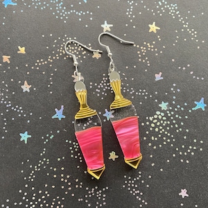 May include: A pair of pink and gold earrings shaped like potion bottles. The earrings have a silver hook closure.