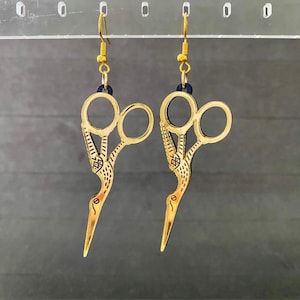 May include: Gold-toned earrings shaped like a pair of scissors with a bird design.