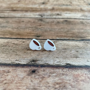 May include: A pair of white coffee cup stud earrings with a brown coffee detail.