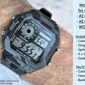 May include: A Casio watch mod kit with a grey camouflage design. The watch face shows the time and date. The kit includes a case, strap, springbars, screws, and gasket. The image text reads "Mod Kit for Casio" and lists compatible models.