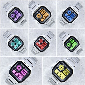 May include: A silver Casio watch with a black face and a multi-coloured digital display. The watch has a silver metal band and a world time function. The watch face displays the time in a digital format with a 12-hour clock and a second hand. The watch also has a date window and a day of the week window.