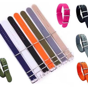 May include: A selection of nylon watch straps in a range of colours: blue, white, black, orange, green, grey, pink, and beige. Each strap has a silver buckle and keepers. These straps are designed for watches.