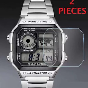 Op de afbeelding: Een zilverkleurig digitaal horloge met een metalen schakelband, voorzien van wereldtijdweergave, 5 alarmen en een 10-jarige batterij. Rechts is een transparante rechthoekige schermbeschermer te zien. Tekst: 2 PIECES en WATCH NOT INCLUDED.
