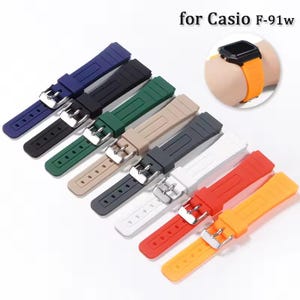 May include: A collection of colorful replacement watch bands for Casio F-91w watches. The bands are in various colors, including blue, black, green, tan, gray, white, red, and orange. Each band has a silver buckle.